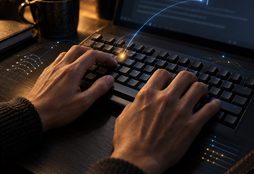 IMAGE: A writer’s hands type on a keyboard as a subtle blue AI signal corrects a single mistaken keystroke without interfering with the writing.